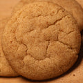 Three round cinnamon sugar cookies stacked on a wooden board with a 'Scratch Cookies' logo printed on it.