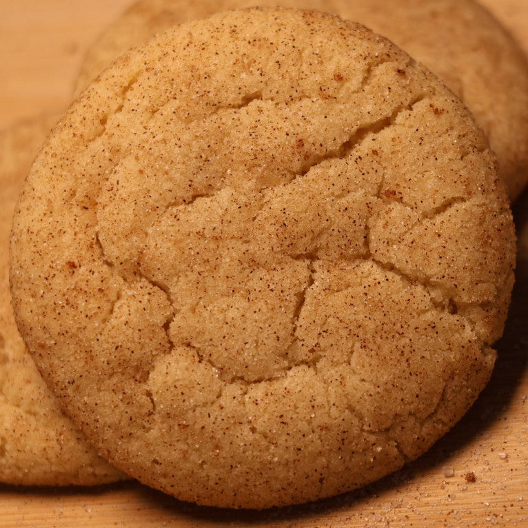 Three round cinnamon sugar cookies stacked on a wooden board with a 'Scratch Cookies' logo printed on it.